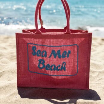 Cabas rouge brodé ‘SEA MER BEACH’ posé sur fond sable clair